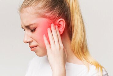 A woman holding her ear with red light coming from it.